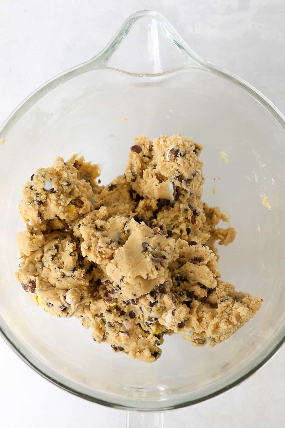 A glass mixing bowl showing the finished cookie dough for a chocolate chip cookie recipe