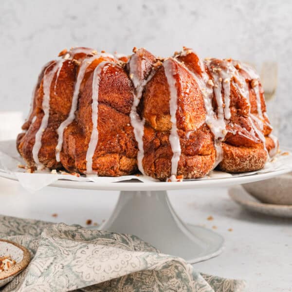 Side view of monkey bread topped with drizzles of vanilla glaze on a cake stand.