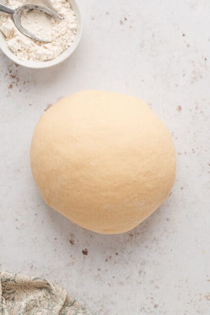 Kneaded dough shaped into a ball on a floured surface.