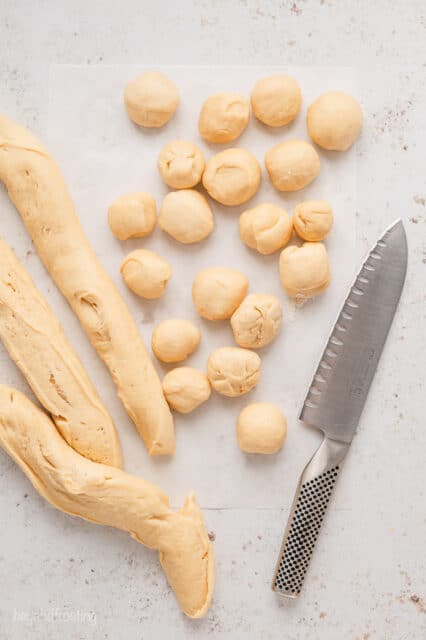 Monkey bread dough divided into ropes and and small balls next to a knife on a countertop.