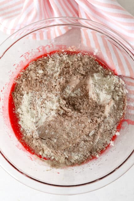 Dry ingredients added to wet red velvet brownie batter in a large glass bowl.