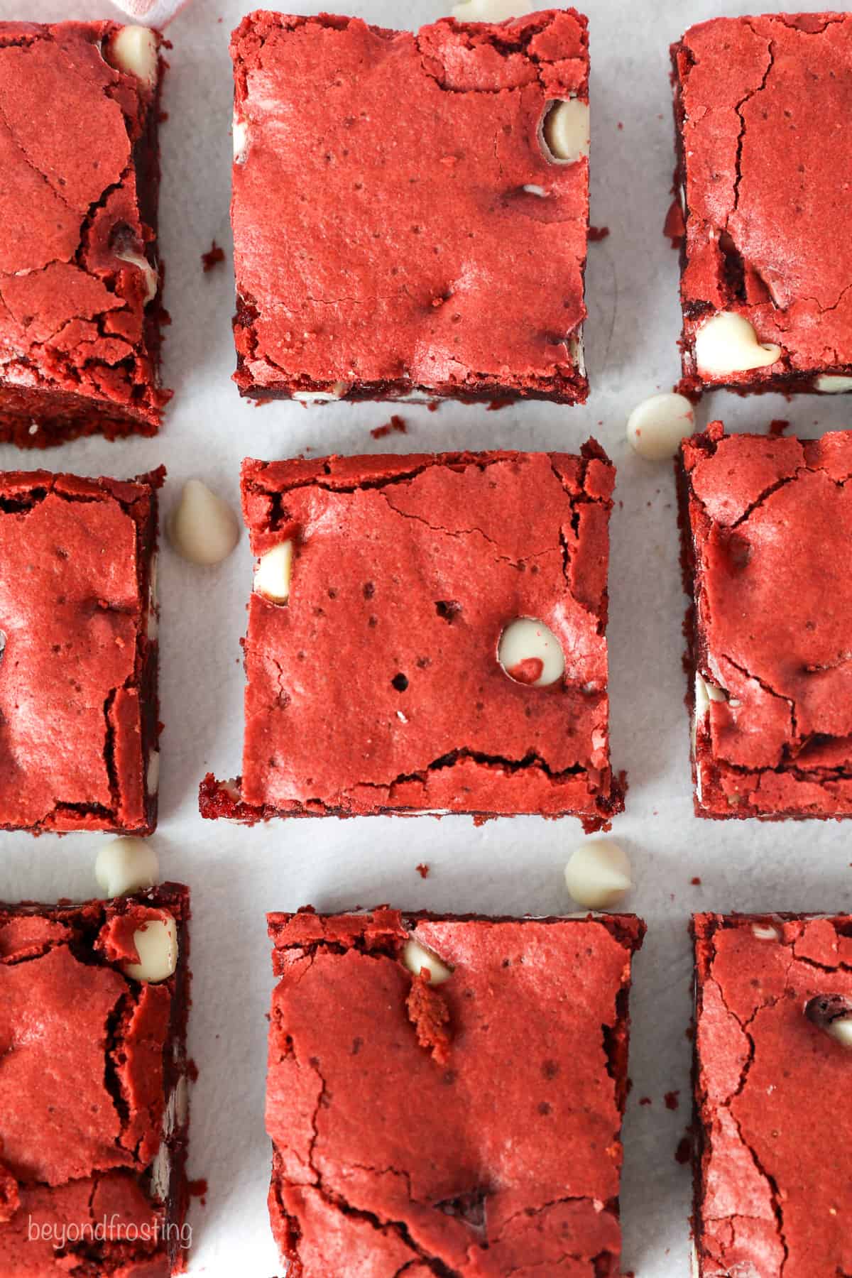 Overhead view of red velvet brownies arranged in rows on a white surface.