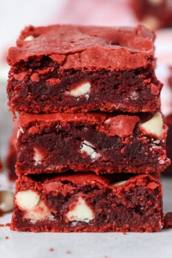 A stack of three red velvet brownies with more brownies in the background.