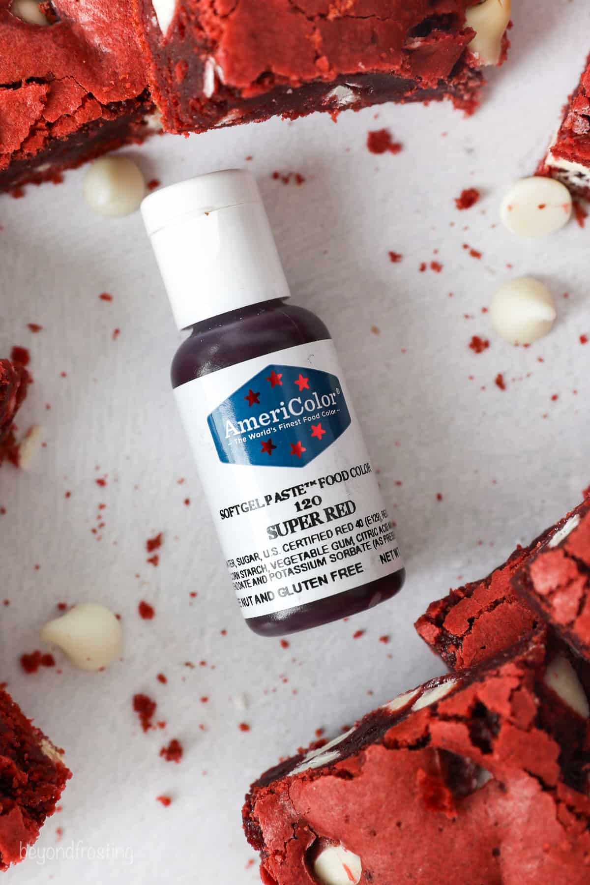 Overhead view of a bottle of AmeriColor red gel food coloring on its side, surrounded by red velvet brownies.