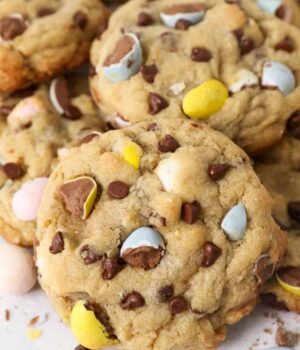 A Cadbury Mini Egg Chocolate Chip Cookie leaning up against a pile of more cookies