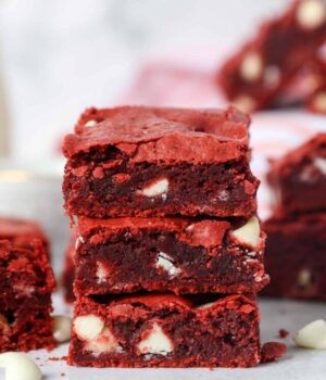 Three red velvet brownies stacked on top of one another, with more brownies in the background.