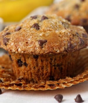 Close up of a partially unwrapped banana chocolate chip muffin with mini chocolate chips around it