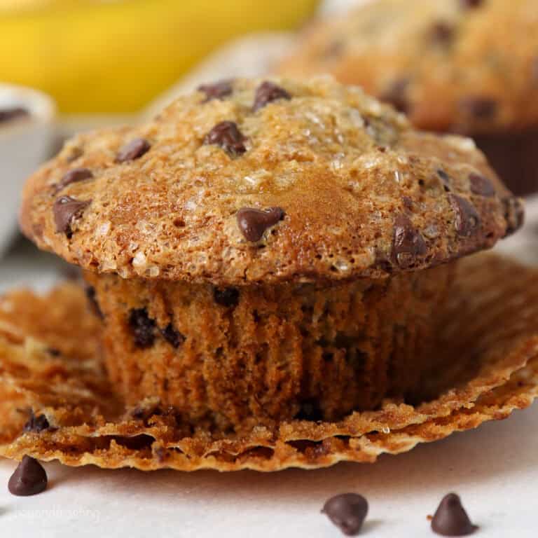 Close up of a partially unwrapped banana chocolate chip muffin with mini chocolate chips around it