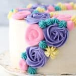 Close up of a buttercream flower cake decorated with pastel frosting rosettes and flowers.