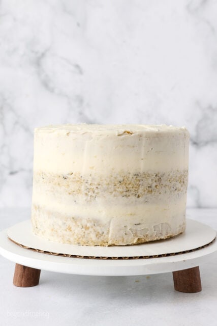 Banana layer cake covered with a crumb coat on a cake stand.