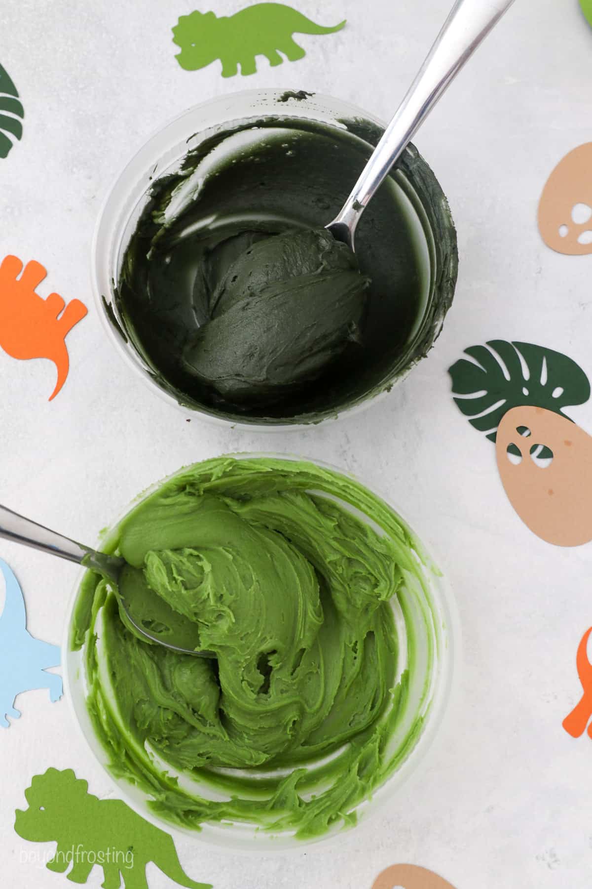 Overhead view of two bowls of frosting dyed dark and lighter shades of green.