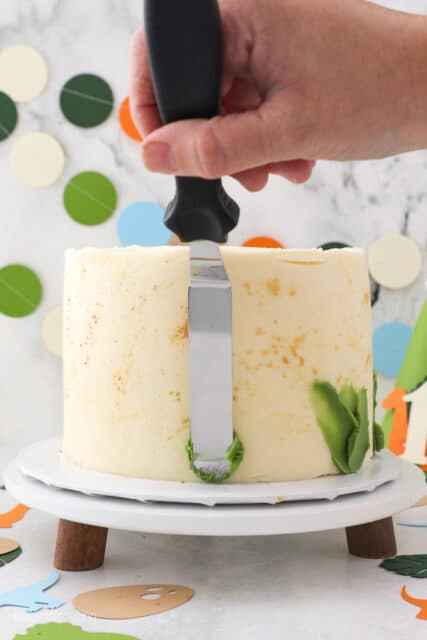An offset spatula spreads light green frosting over the side of a gold-splattered cake to create a skirt.