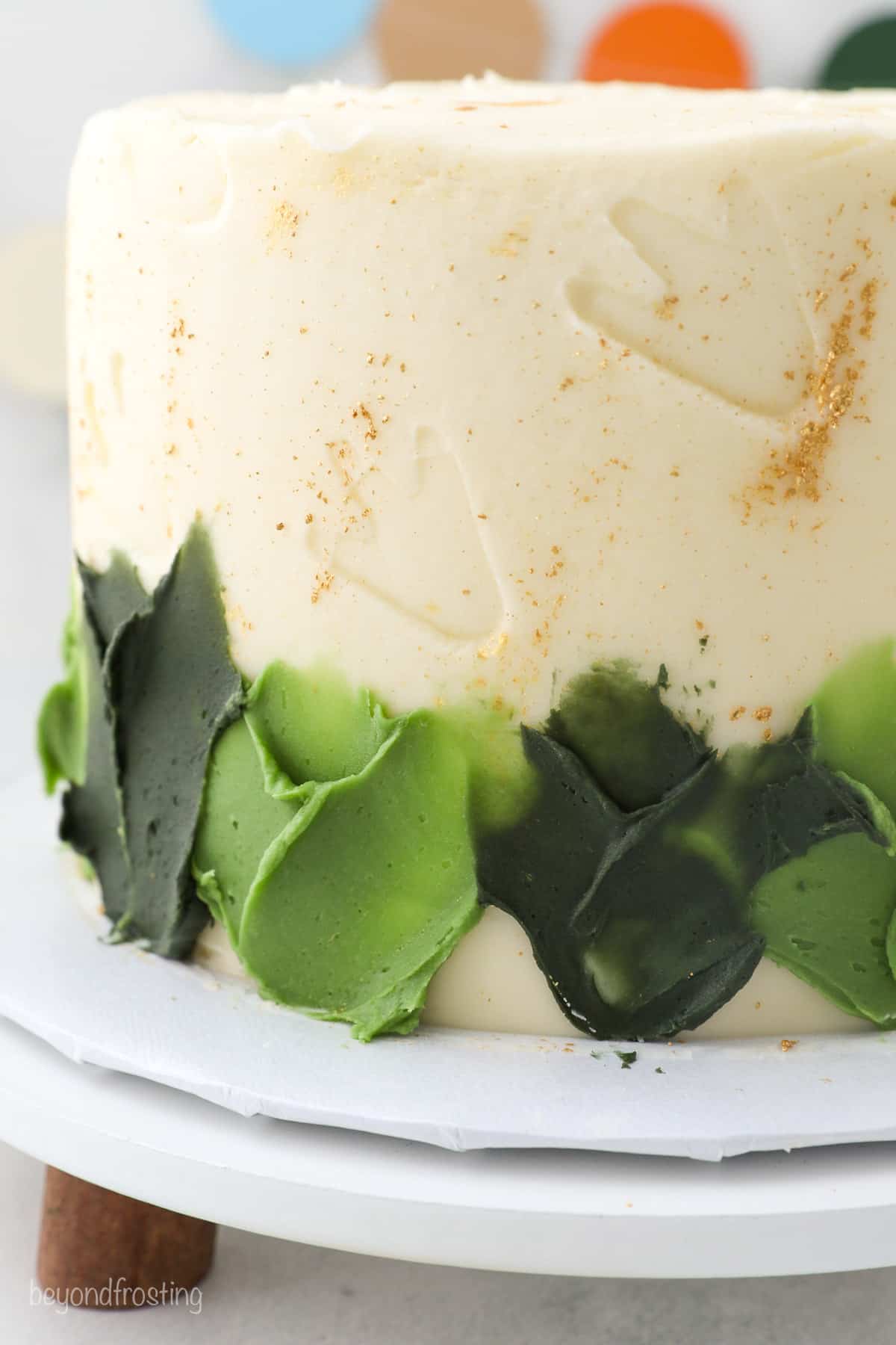 Close up of a skirt made with green colored buttercream on a gold-splattered dinosaur cake.