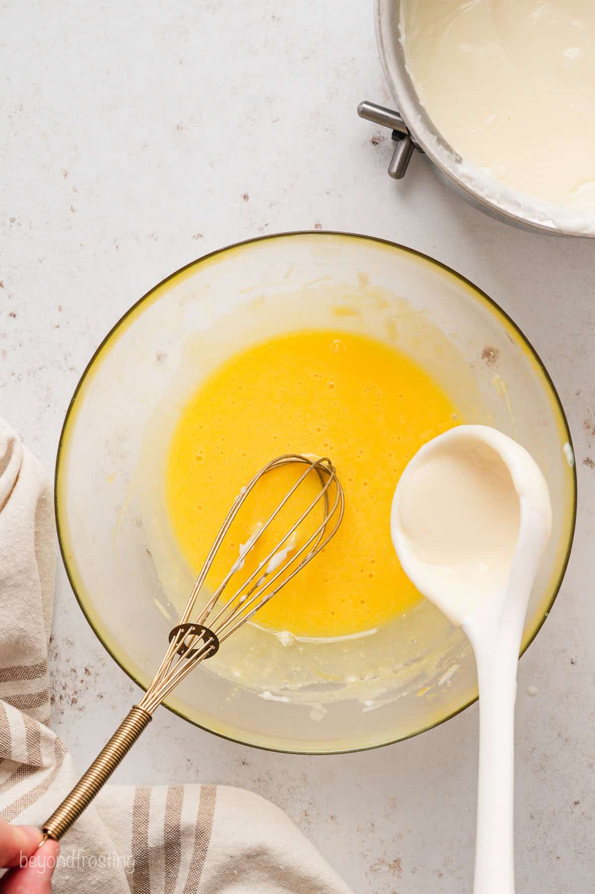 Warm pudding mixture added to a bowl of whisked egg yolks to temper them.