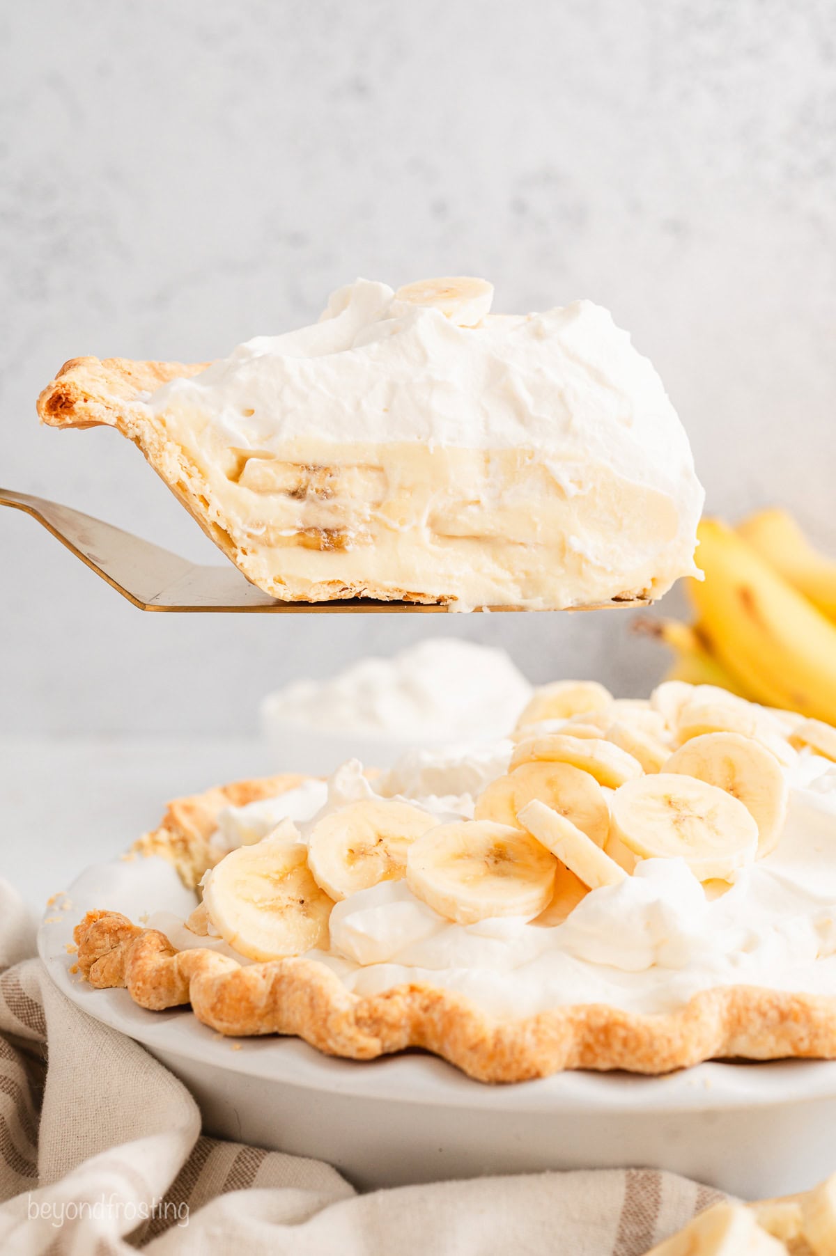 A slice of banana cream pie lifted from the rest of the pie with a cake server.