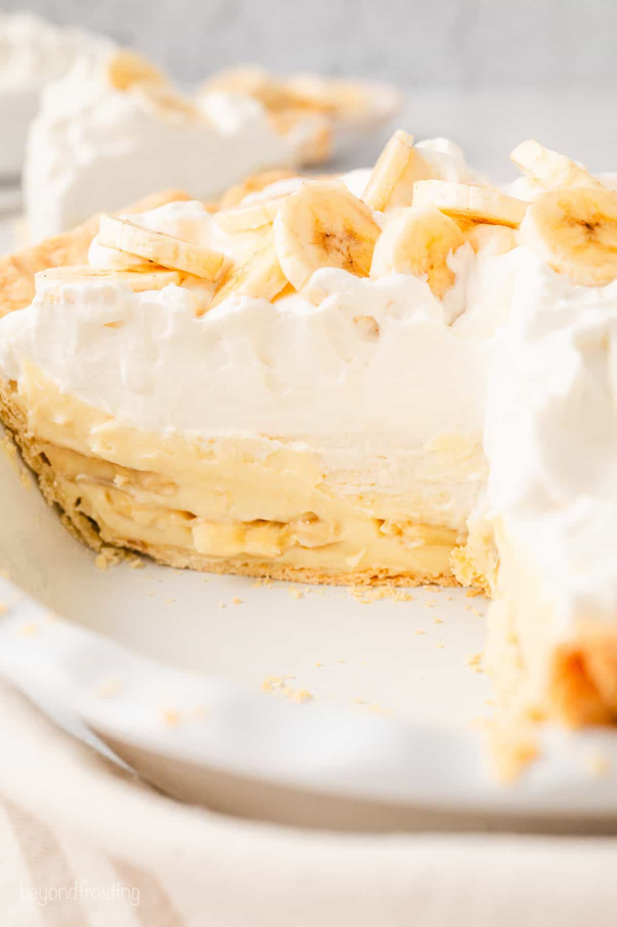 Banana cream pie topped with banana slices in a pie plate, with a slice missing.