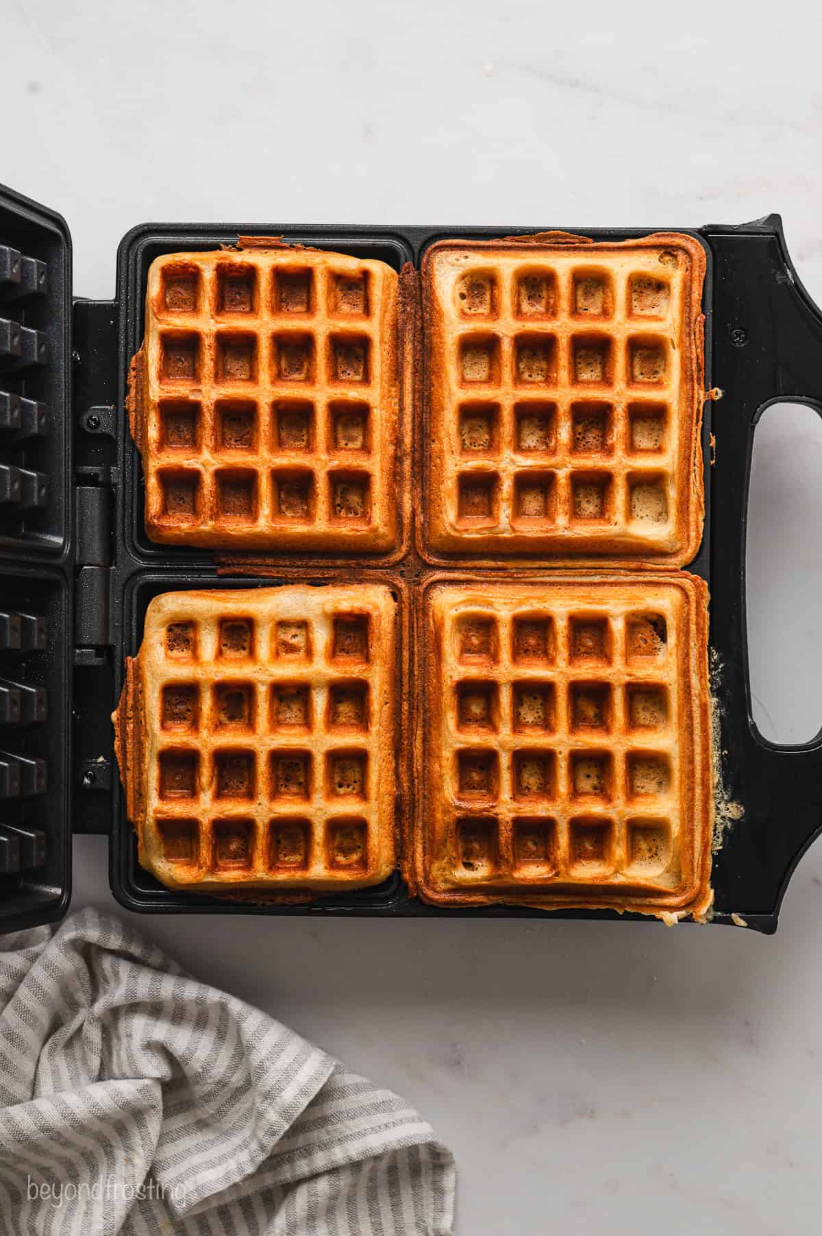 Four cooked waffles inside a waffle iron.