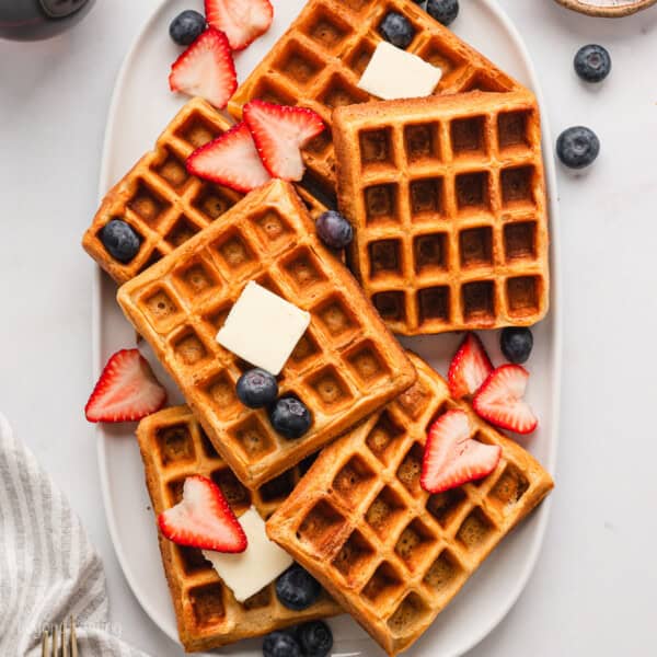 Overhead view of buttermilk waffles arranged on a platter, topped with butter and fresh strawberries and blueberries.