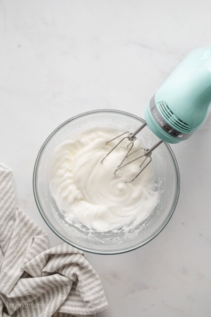 A hand mixer resting in a bowl of whipped egg whites.