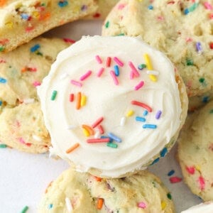 Overhead view of a frosted funfetti cake mix cookie resting on top of a pile of cookies.