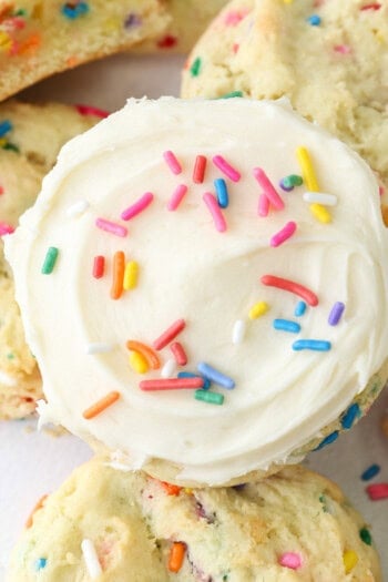 Overhead view of a frosted funfetti cake mix cookie resting on top of a pile of cookies.