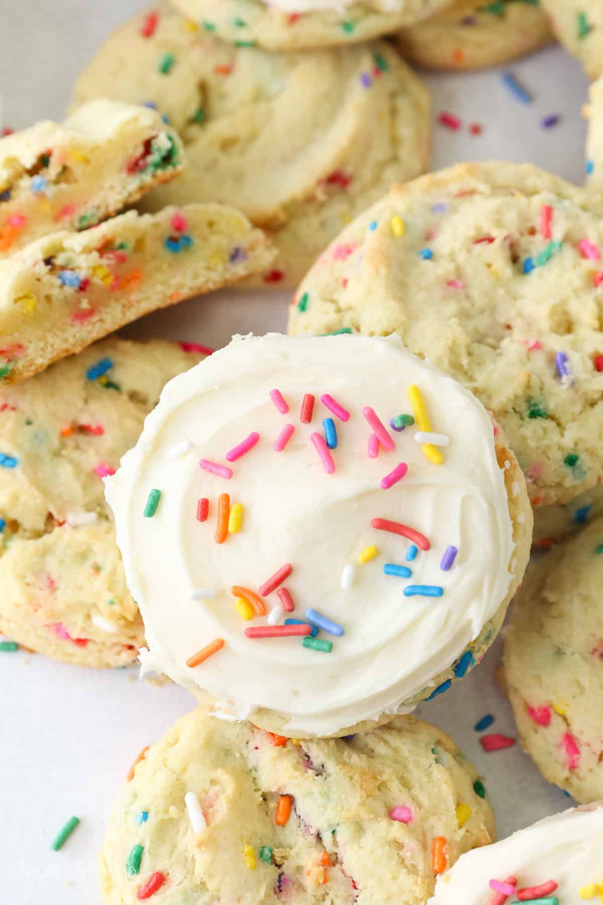 Overhead view of a frosted funfetti cake mix cookie resting on top of a pile of cookies.
