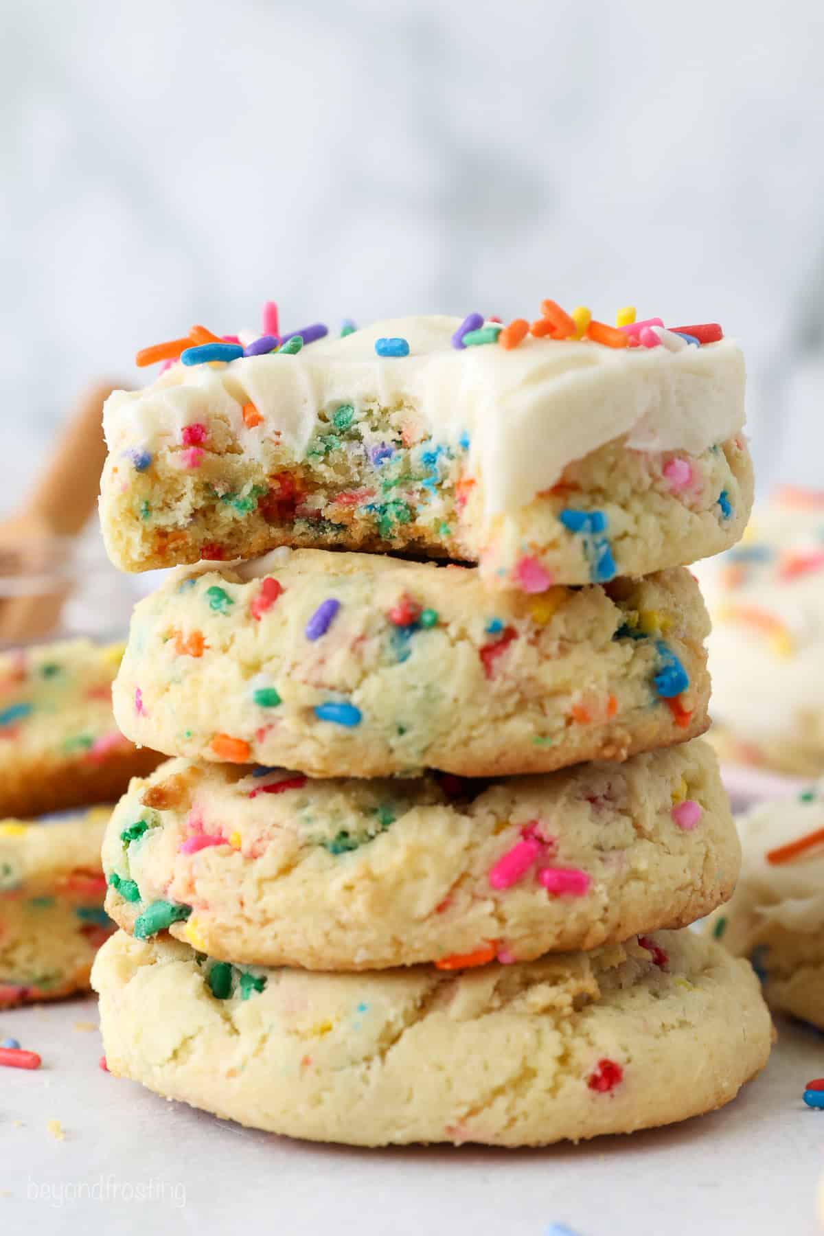 A stack of funfetti cookies, with a bite missing from the frosted cookie at the top of the stack.