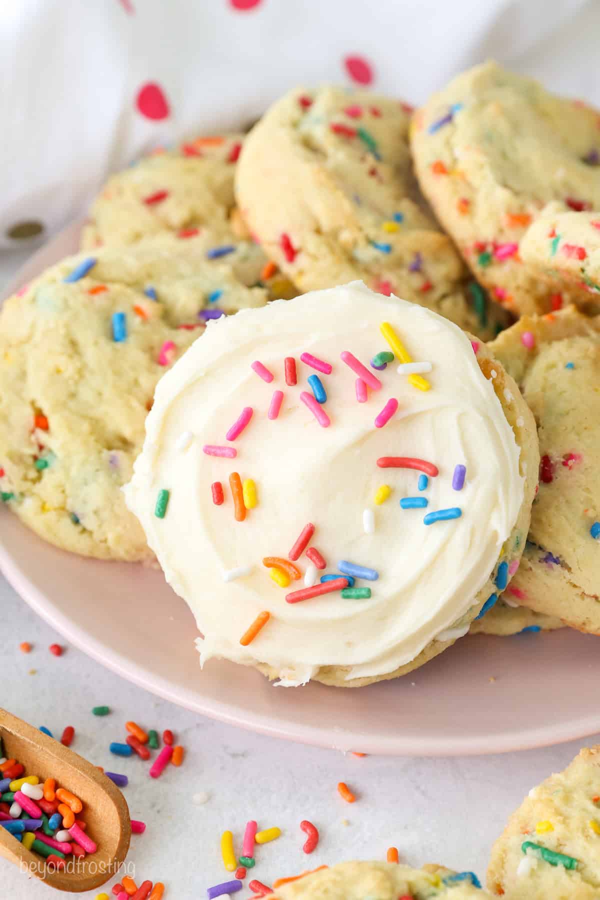 A frosted funfetti cake mix cookie leaning against a pile of cookies n a plate.