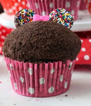 Close up of a Minnie Mouse cupcake topped with a pink candy bow.