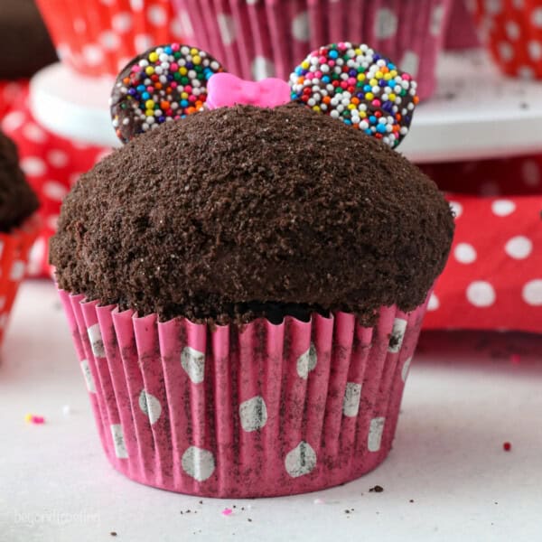 Close up of a Minnie Mouse cupcake topped with a pink candy bow.