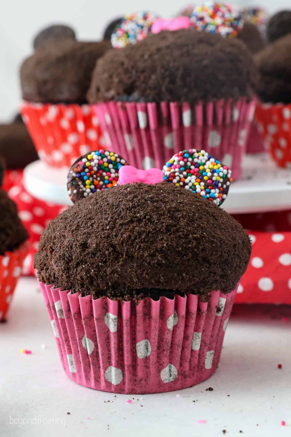 Close up of a Minnie Mouse cupcake with more cupcakes on a plate in the background.