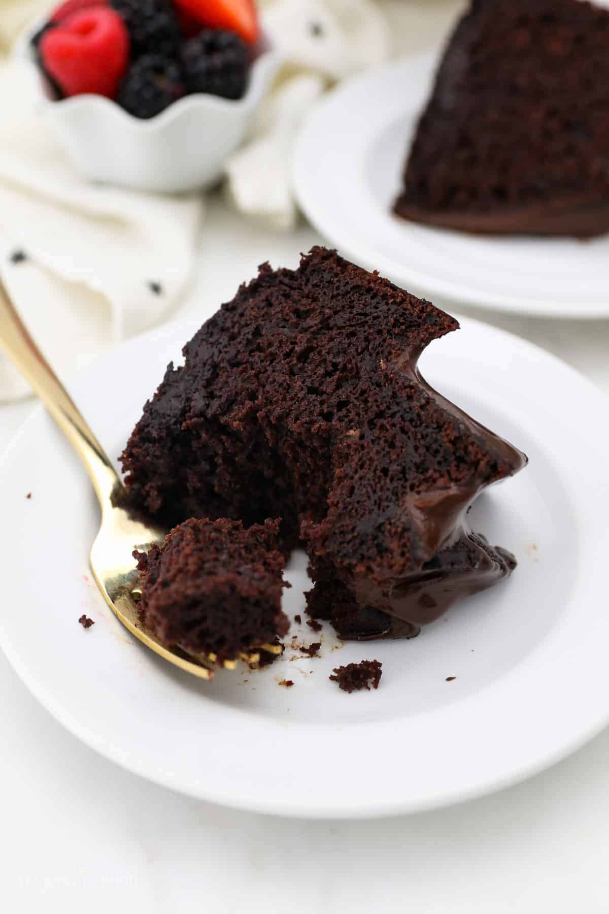 A forkful of chocolate bundt cake resting next to a slice of cake on a white plate.