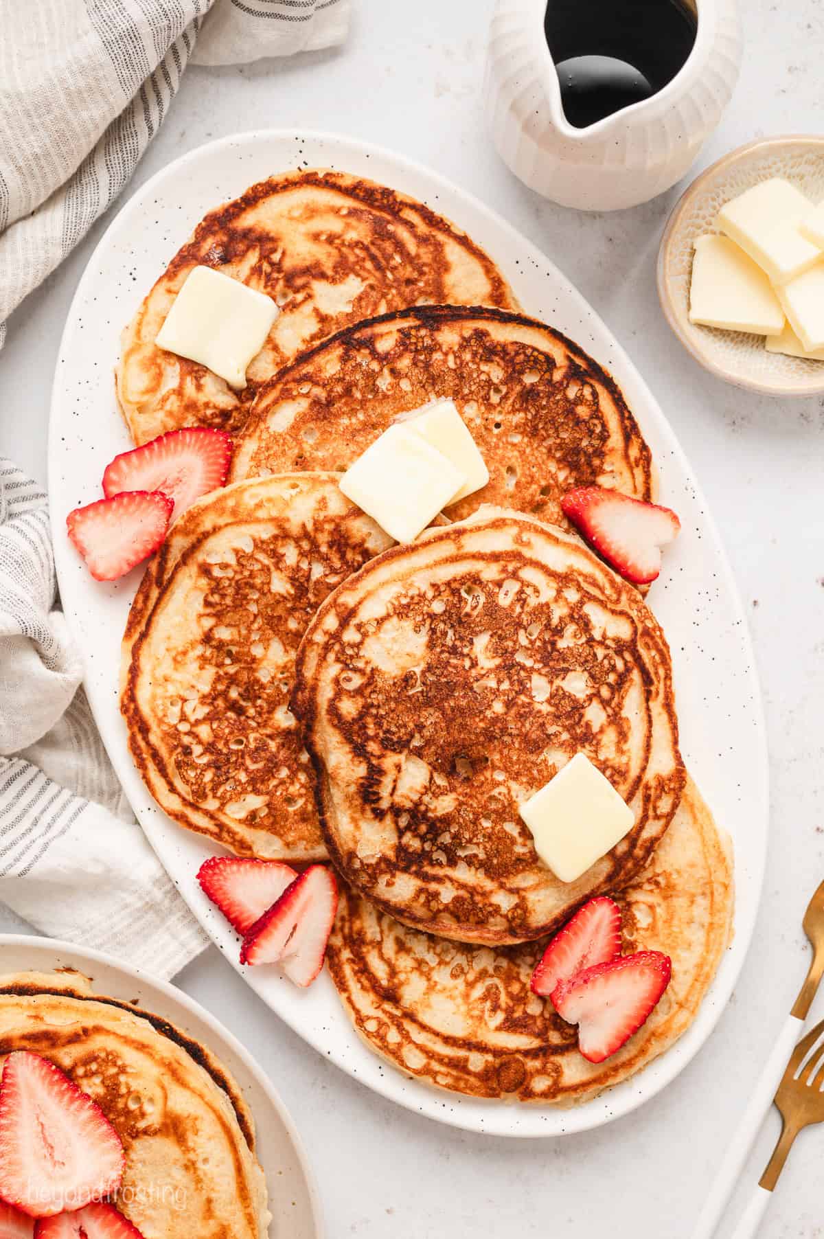 Overhead view of assorted buttermilk pancakes on a large serving platter, topped with pats of butter and garnished with fresh strawberries.