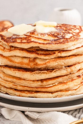 A stack of buttermilk pancakes topped with pats of butter on a plate.