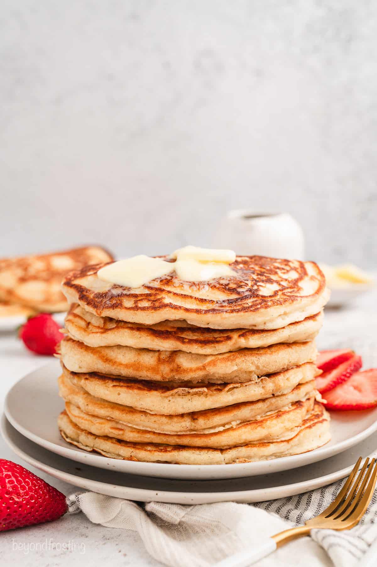 A stack of buttermilk pancakes topped with pats of butter on a plate.