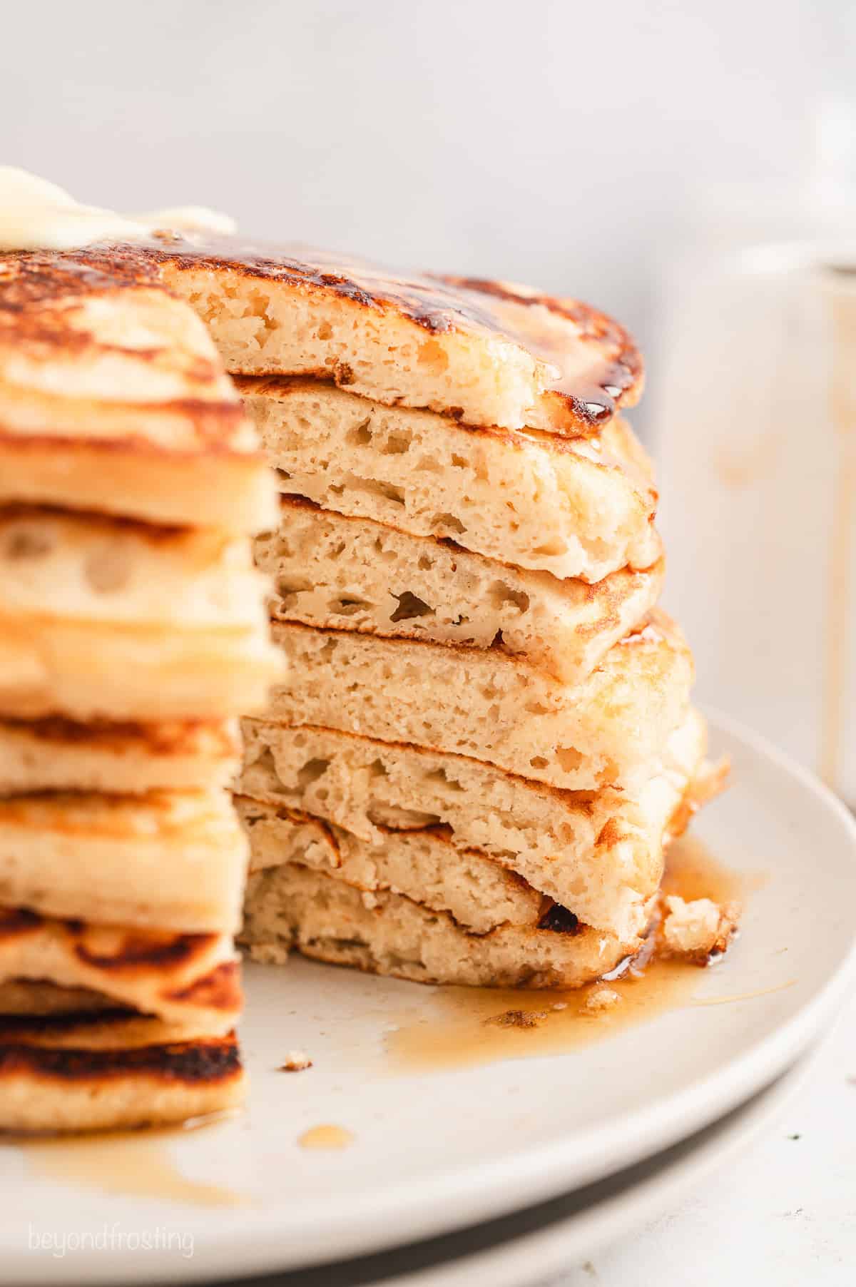 A stack of pancakes with a slice missing, drizzled with maple syrup on a white plate.