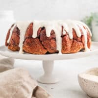 Cinnamon roll monkey bread covered with vanilla icing on a white cake stand.