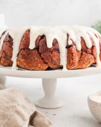 Cinnamon roll monkey bread covered with vanilla icing on a white cake stand.