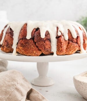 Cinnamon roll monkey bread covered with vanilla icing on a white cake stand.