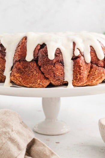 Cinnamon roll monkey bread covered with vanilla icing on a white cake stand.