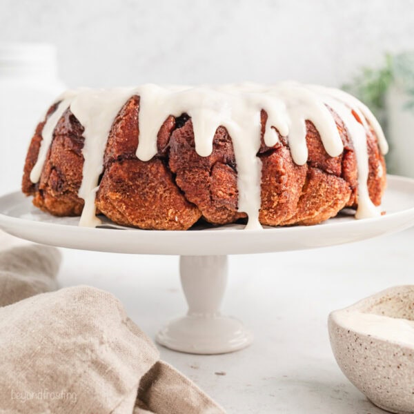 Cinnamon roll monkey bread covered with vanilla icing on a white cake stand.