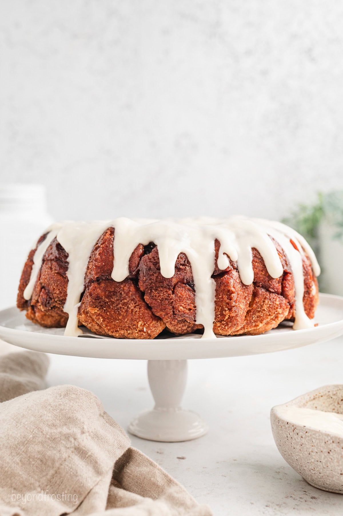 Cinnamon roll monkey bread covered with vanilla icing on a white cake stand.