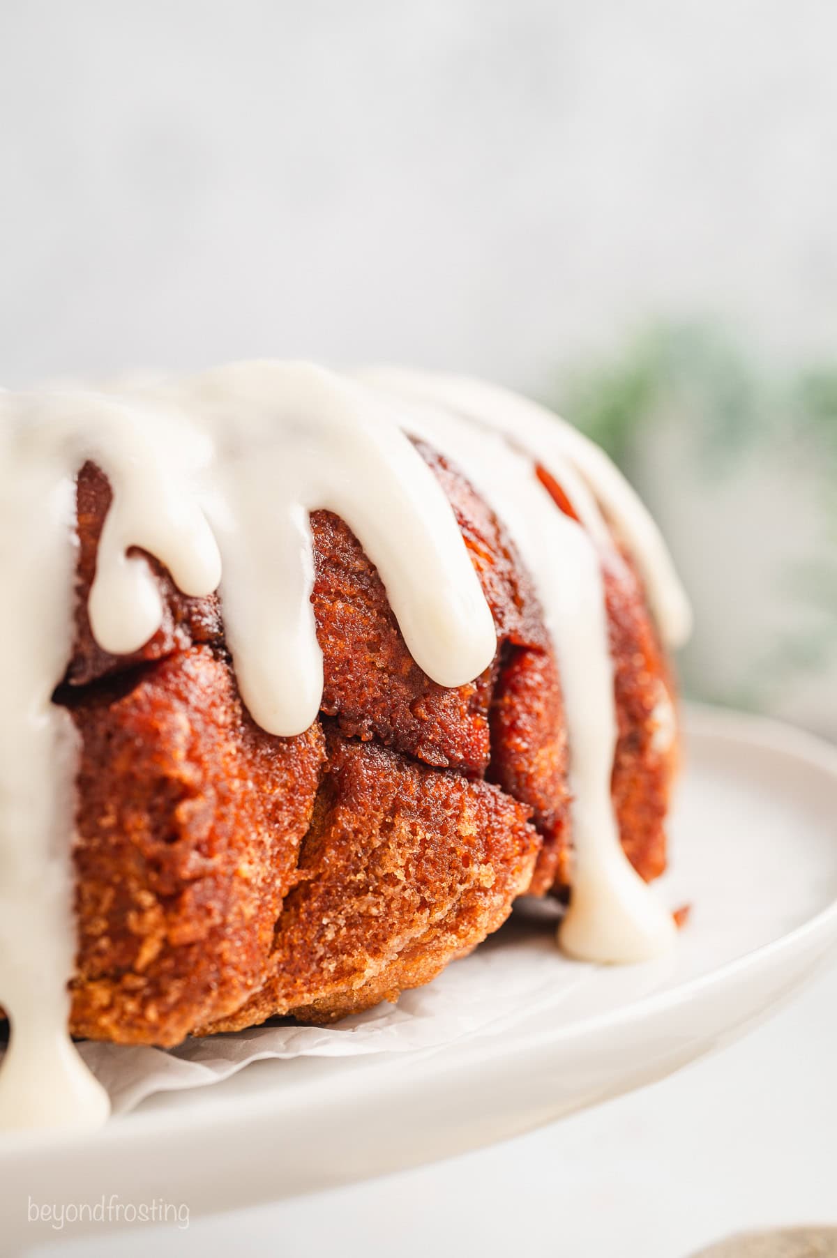 Close p of cinnamon roll monkey bread covered with vanilla icing on a white cake stand.