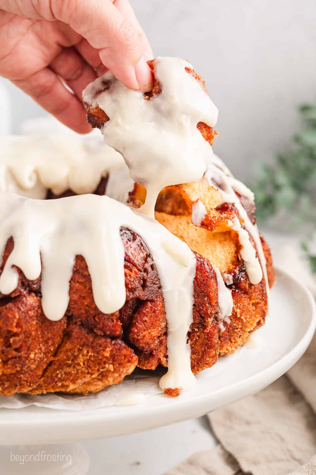 Cinnamon roll monkey bread covered with vanilla icing on a white cake stand.