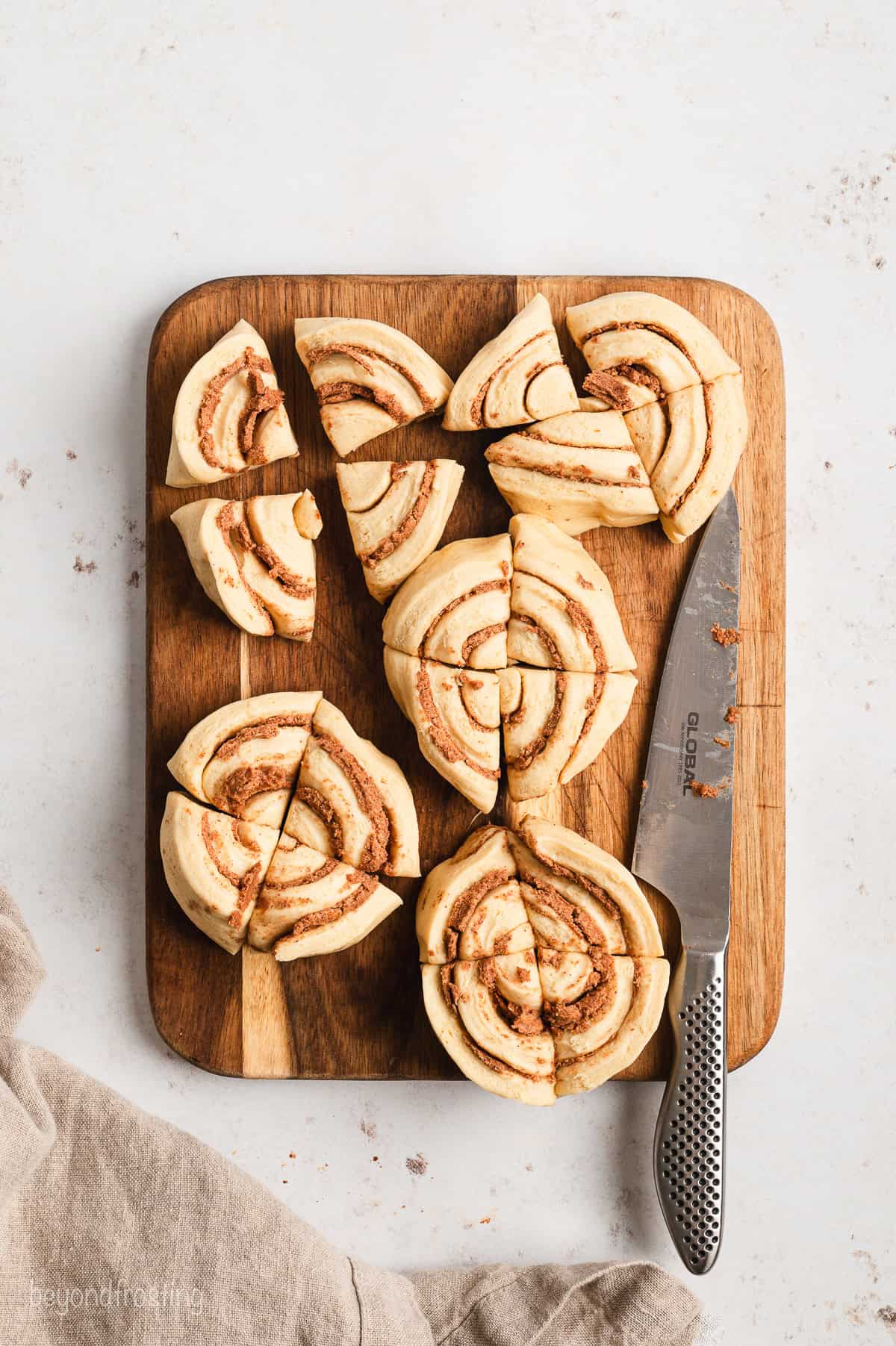 Overhead view of unbaked Pillsbury Grands cinnamon rolls cut into quarters on a wooden cutting board next to a knife.