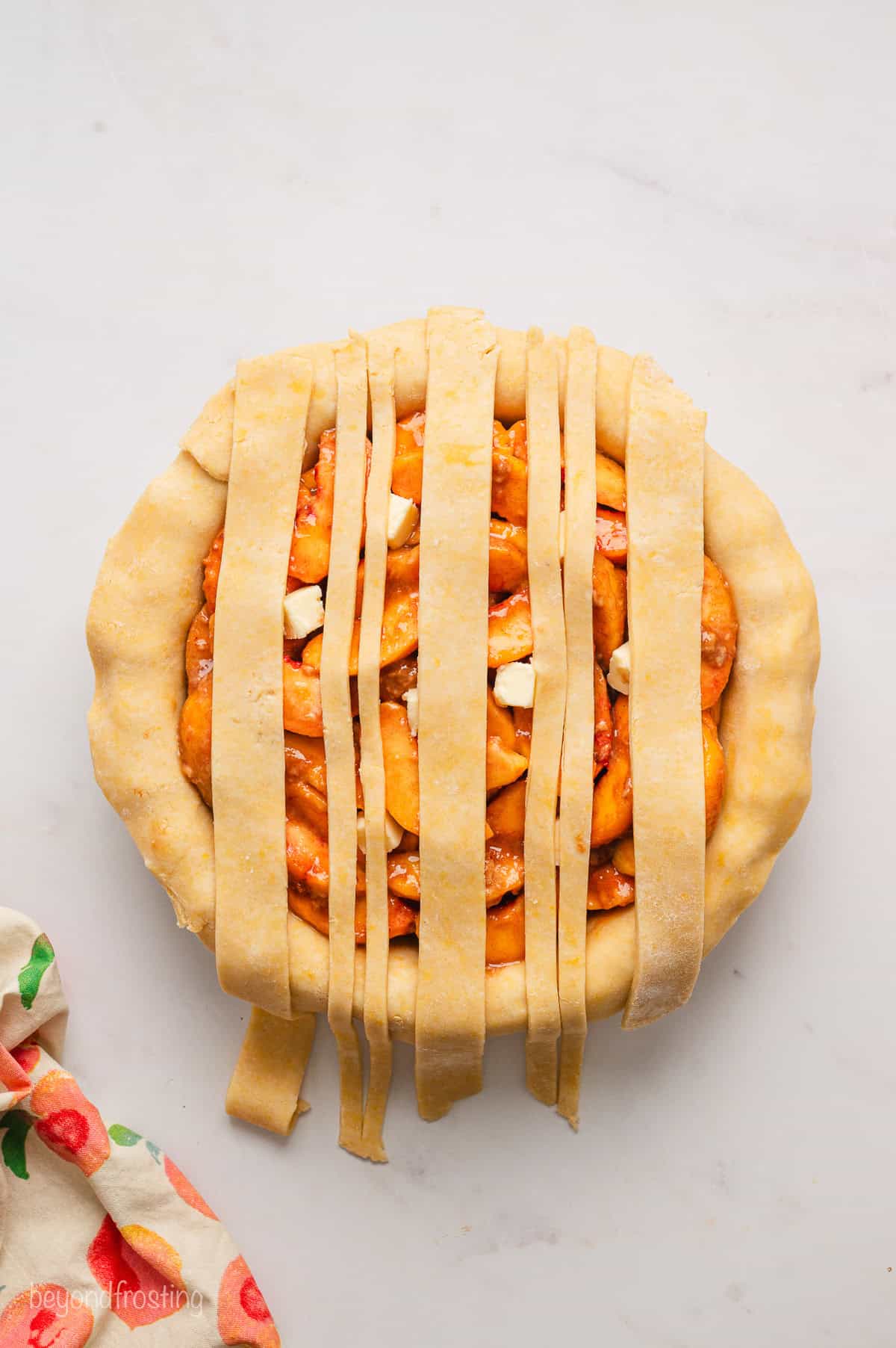 Overhead view of a lattice crust being assembled over a peach pie.