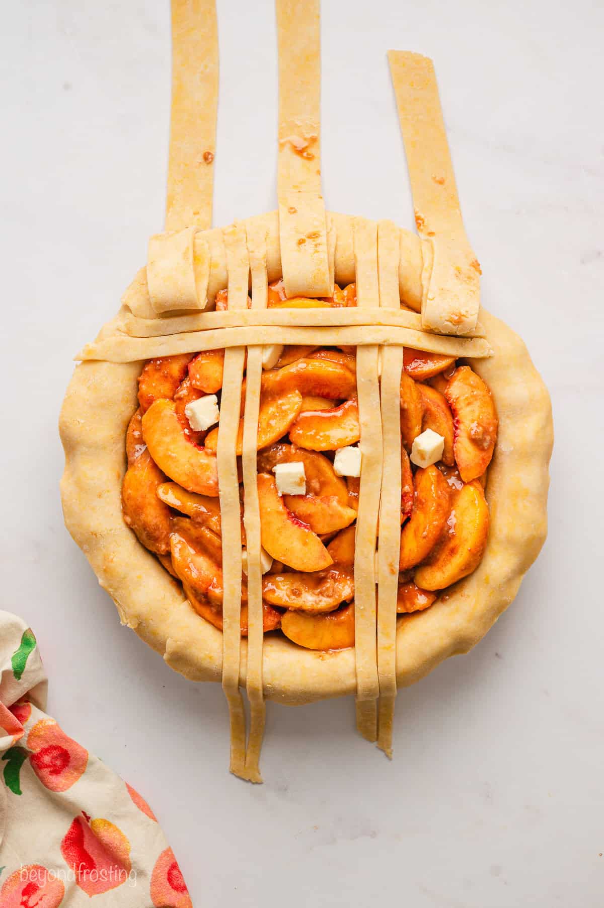 Overhead view of a lattice crust being assembled over a peach pie.