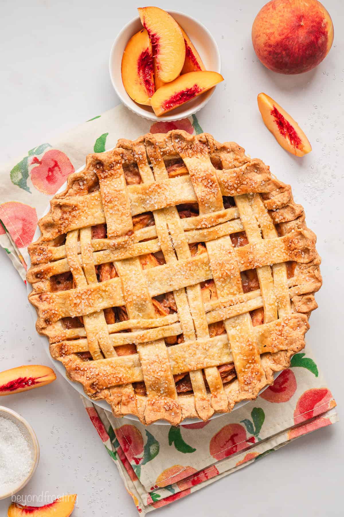 Overhead view of a peach pie with a lattice crust next to a bowl of peach slices.