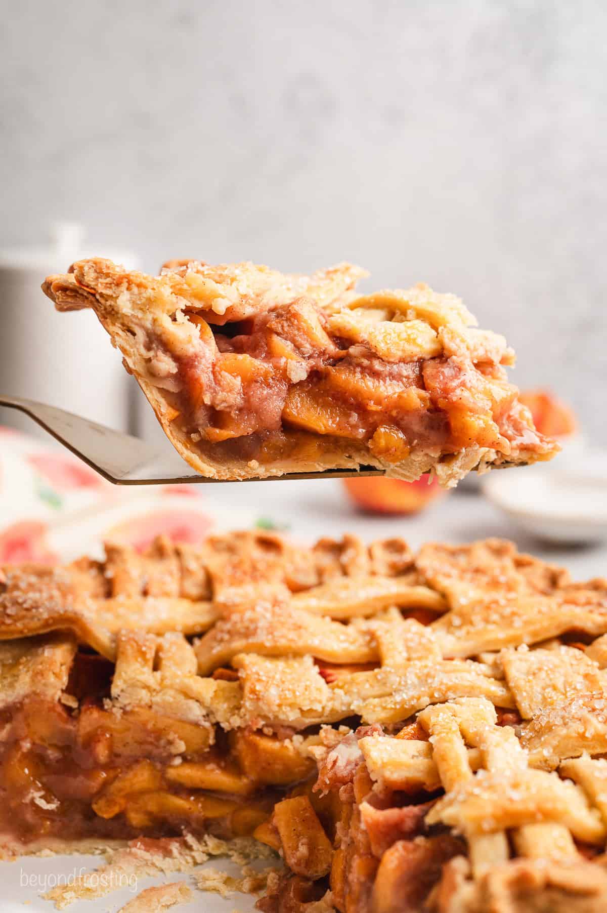 A slice of peach pie being lifted above the rest of the pie with a cake server.