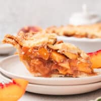 A slice of peach pie on a white plate, with the rest of the pie in the background.